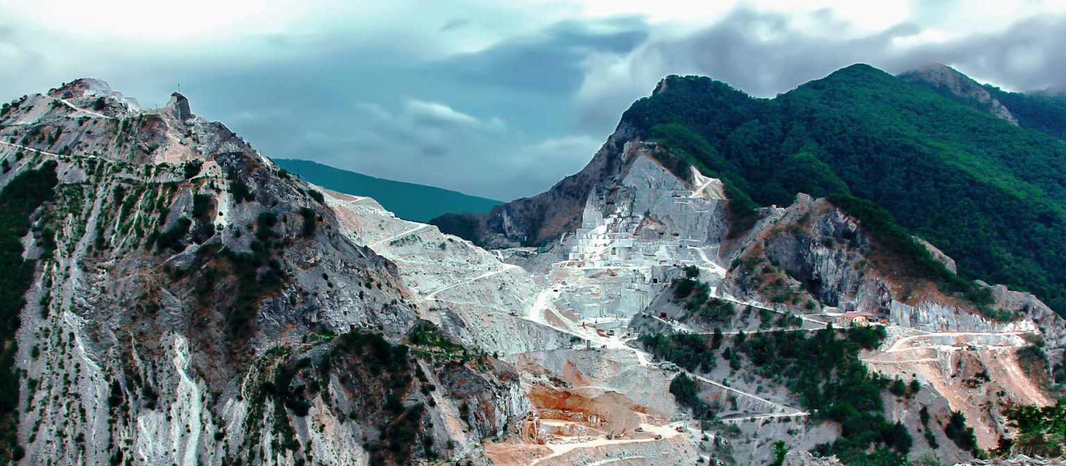 Steinbruch mit weißem, italienischen Carrara Marmor der Links im Bild mit grünem Wald bedeckt ist.