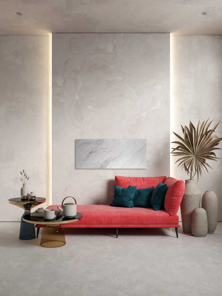 Wohnzimmer mit hoher Decke stilvoll eingerichtet mit roter Couch über der eine helle Natursteinheizung Volakos an der Wand montiert ist.