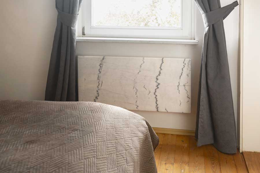 Nachtspeicherheizung ersetzen - Infrarotheizung Natursteinheizung vor Fenster in einem Schlafzimmer wo früher ein Nachtspeicherofen stand.